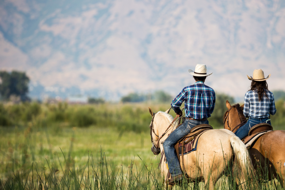a couple horseback riding from behind overlooking wide open field and mountains of Utah wilderness